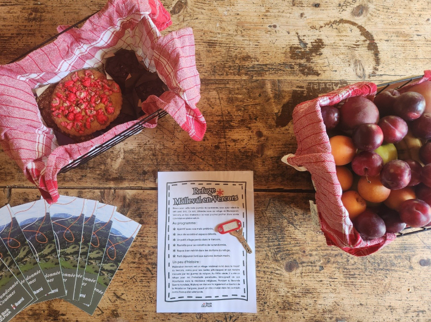 une table avec de la nourriture, des cartes IGN et un message de bienvenue avec les clés du refuge